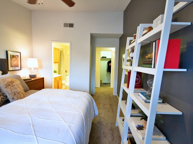 This image shows a master bedroom with direct access through the bathroom and closet. It offers spacious floor plans, oversized windows with blinds, a huge shelf, and an ideal ceiling fan.